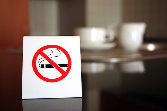 a no smoking sign sits on a table with coffee cups in the background
