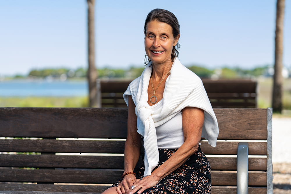 A woman sits on a wooden bench on a pier with marsh and river behind her