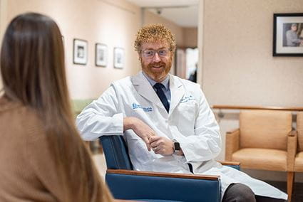 a woman wearing a white doctor's coat and holding a clipboard talks with another person