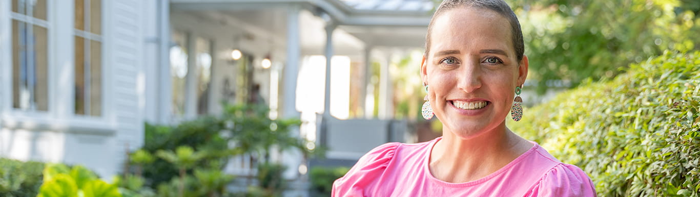 a woman with nearly bald head and bright pink shirt smiles