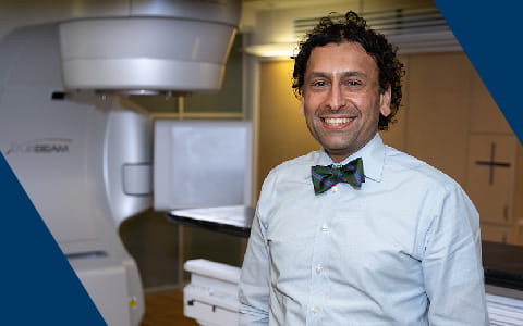 a man wearing a bow tie stands next to radiation oncology equipment