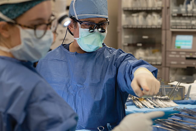a man in surgical scrubs and mask points in an operating room while a woman dressed the same looks where he's pointing