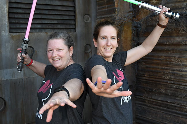 Two women with huge grins on their faces wield light sabers