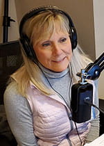 Janis Newton wears headphones and sits in front of a microphone