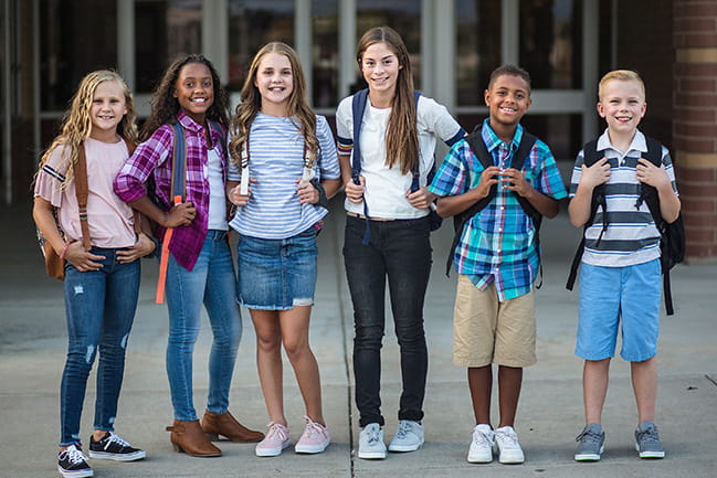 diverse group of preteen kids wearing backpacks in front of a school