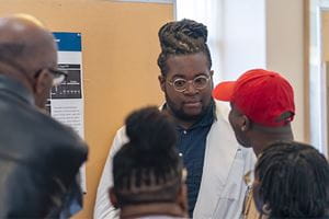 a student talks about his research poster as a group of people stand around him