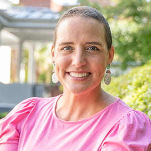 a smiling woman with a nearly bald head wearing a light pink shirt
