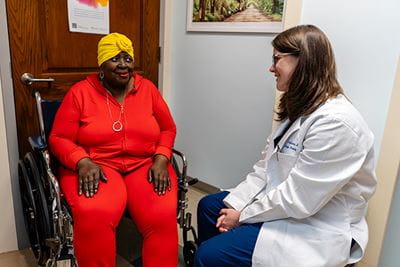 a doctor talks to a patient sitting in a wheelchair in an exam room