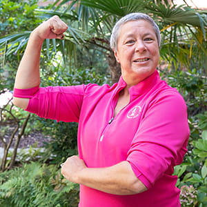 a woman wearing a bright pink shirt flexes her right arm
