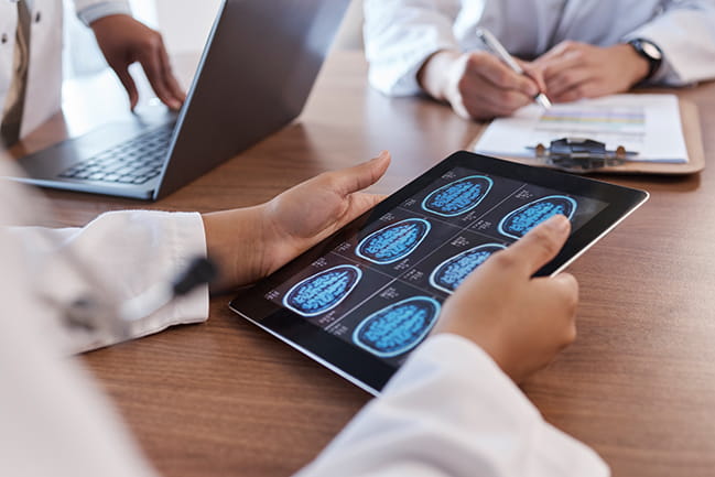 a group of doctors huddle around a table looking at a tablet showing brain scan images
