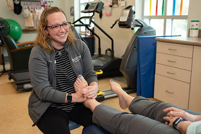 smiling physical therapist works on a patient's foot