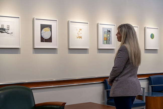 a woman stands looking at a row of framed artwork hanging on the wall of a patient waiting area