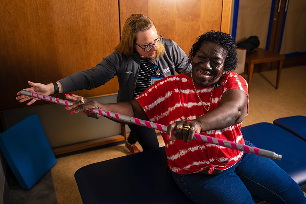 Dr. Katie Schmitt guides a patient doing a physical therapy exercise with a metal bar