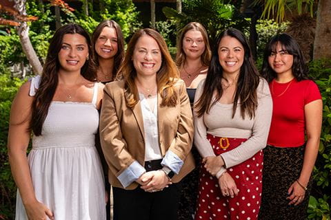 a group of six smiling women stand together for a photo outside