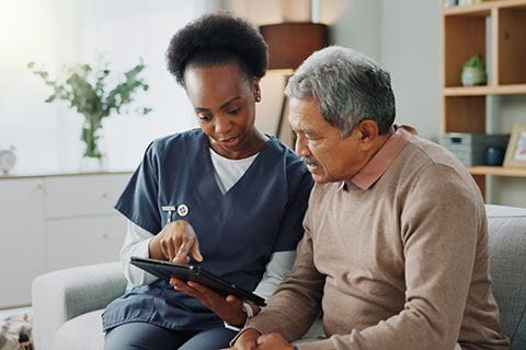 image of a young female home health nurse taking an older man's blood pressure while they sit on a couch in a home