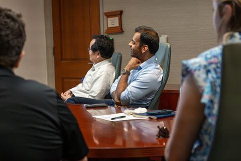 a group of people sit at a conference table watching a presentation on a screen at the front of the room