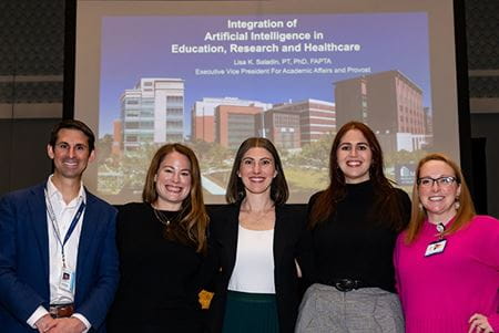 a group of people stand together in front of a projector screen at a symposium