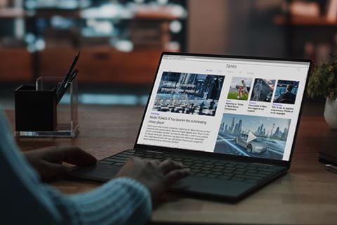 person sitting at a desk looks at a news website on a laptop 