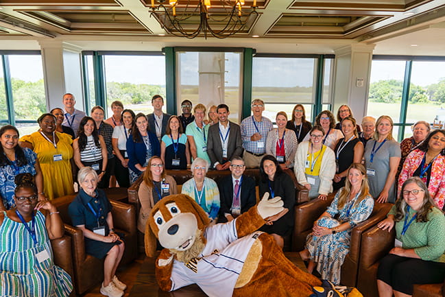 large group of attendees at the SCOR Symposium seated and standing with Charleston RiverDogs mascot lying in front of the group