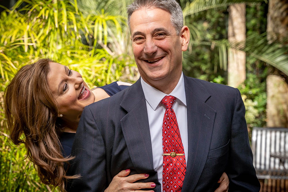A man laughs with wife while standing outside.