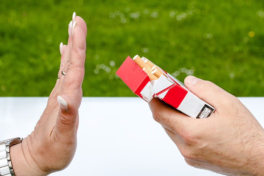 A hand rejects another hand holding an open pack of cigarettes