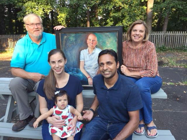 Members of the Olson family sit together and hold a painting of William Olson, the inspiration for the Rally Foundation 