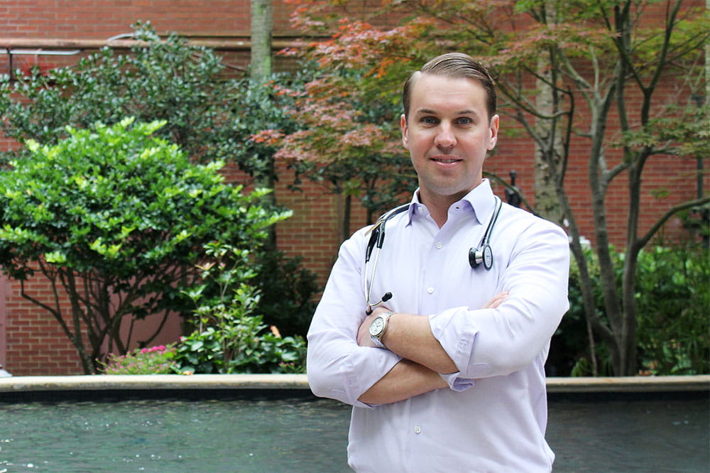Dr. Brian Greenwell stands outside in a garden with a stethoscope around his neck