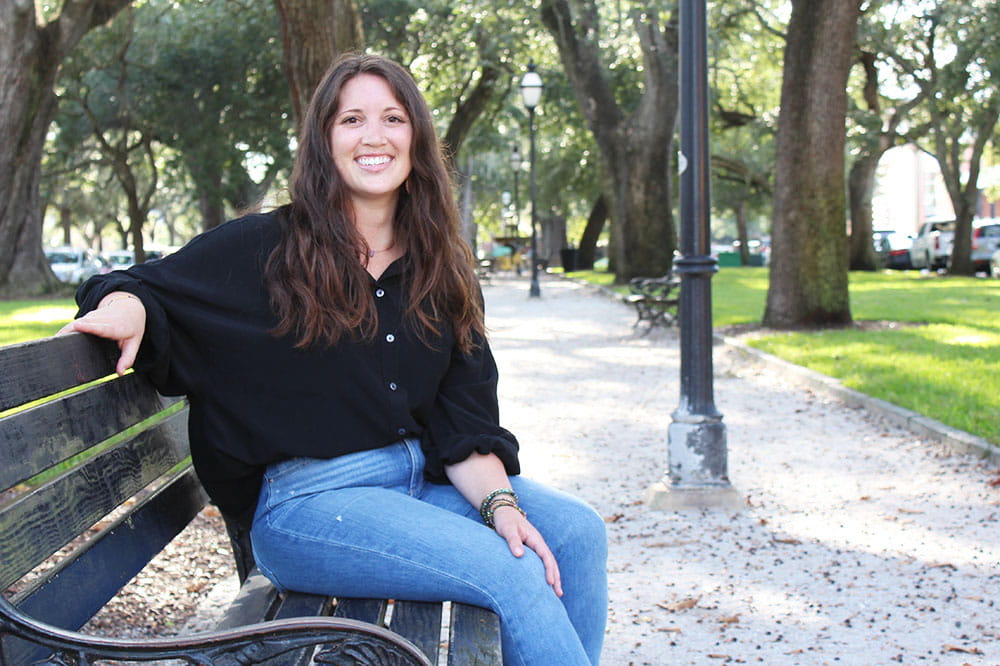Kelly Bulak sits on a park bench with trees in the background