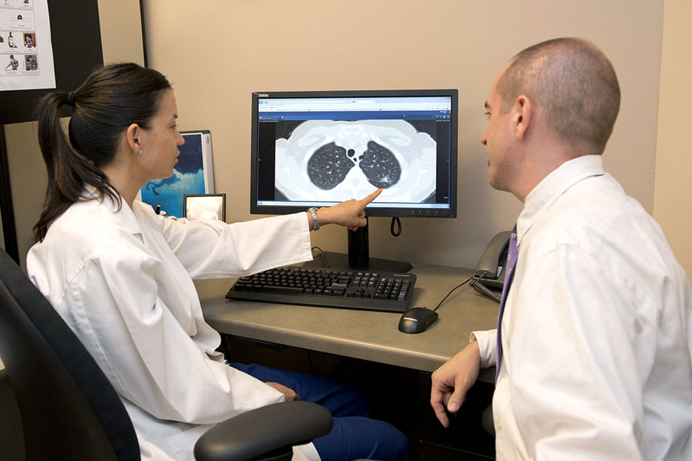 Dr. Nichole Tanner and Dr. Benjamin Toll look at a computer showing a lung cancer scan