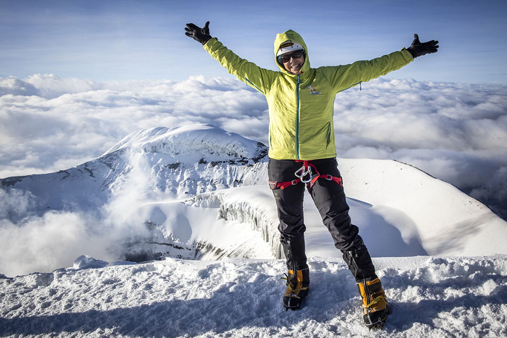 Cokie Cox stands on top of a snowy mountain in Ecuador with both arms raised