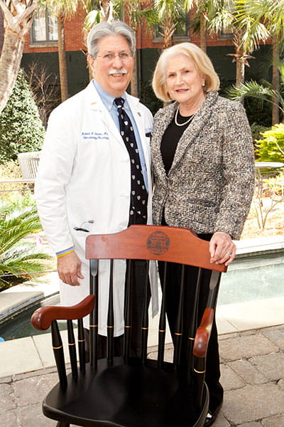 Robert and Charlene Stuart stand in front of a wooden chair