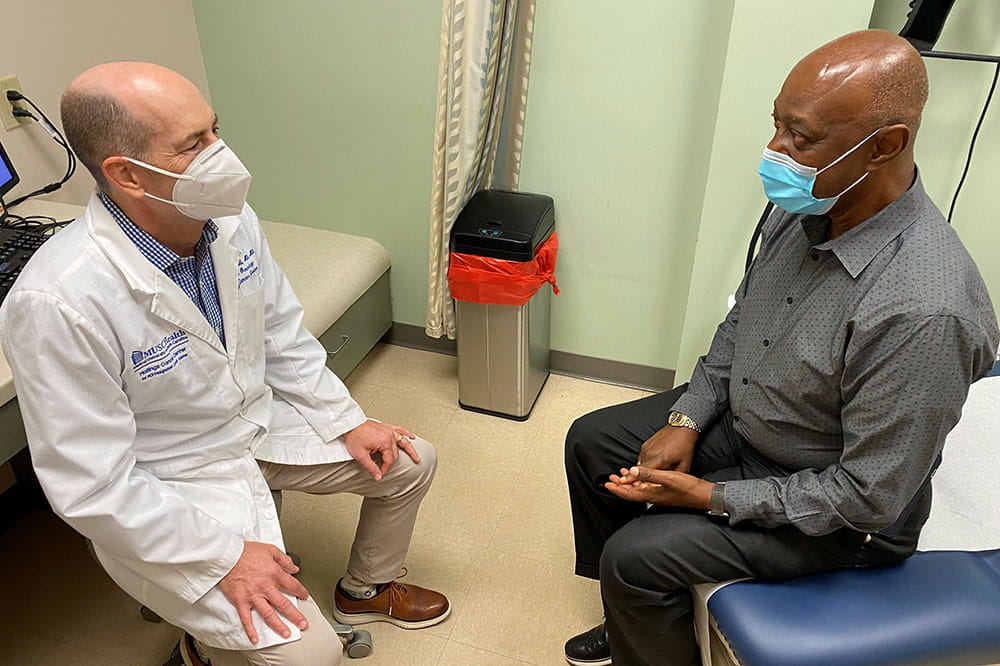 Dr. David Marshall talks with Larry Ferguson in an exam room wearing masks