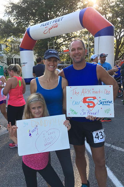 Bruce Dales at a race finish line with his wife and daughter holding signs of support