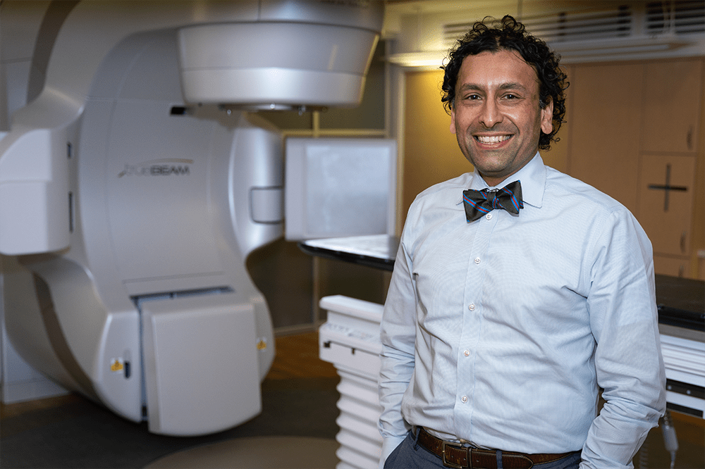 Bhisham Chera, M.D., stands in front of a radiation machine.