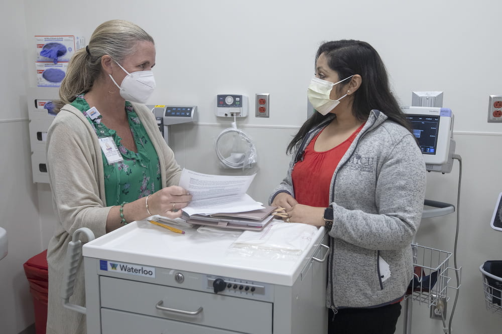 Dr. Carrie Cormack and student Parag Raychoudhury talk while wearing masks.