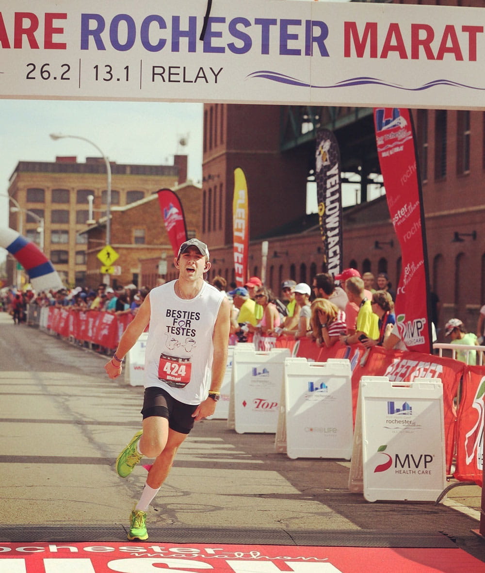 a man runs triumphantly under a sign that says Rochester Marathon