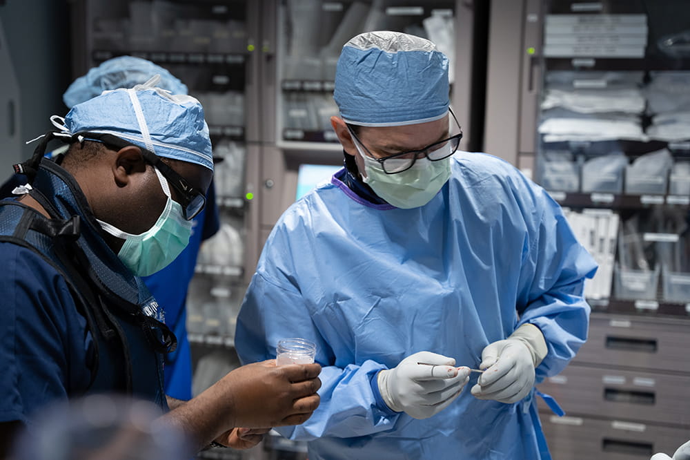 a man in a surgical scrubs works with a man in a lead apron in an operating room