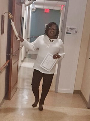 a woman stands in a hospital hallway and rings a bell attached to the wall 
