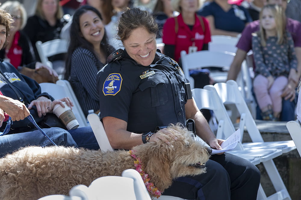 A female police officer laughs as a fluffy dog approaches