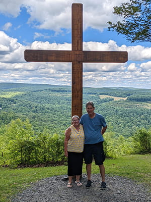 a man and woman stand on a hill in front of a large cross
