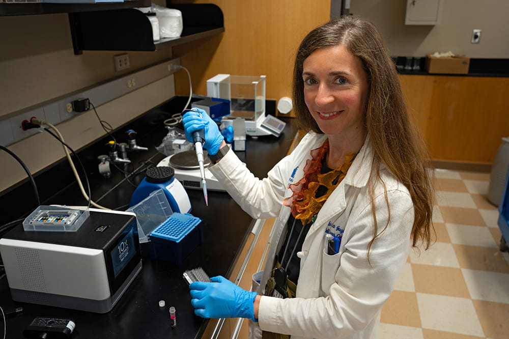 a woman in white lab coat and blue gloves smiles up at the camera