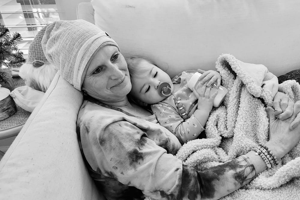 black and white image of a woman with a knit cap on her head snuggled on sofa with a toddler girl snuggling with her