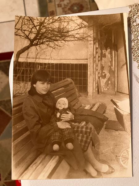 An old, yellowed photo of a woman sitting on a park bench with her toddler daughter in her lap