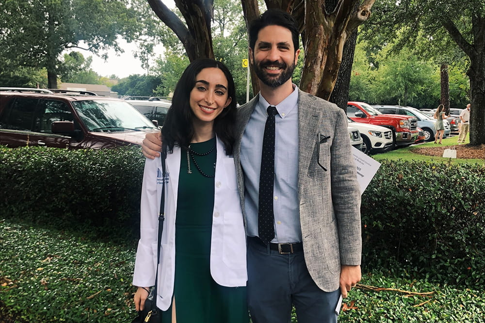 a man in a sport coat poses with a young woman in a white medical student coat