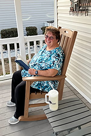 a woman sits on a rocking chair on her porch and smiles up at the camera