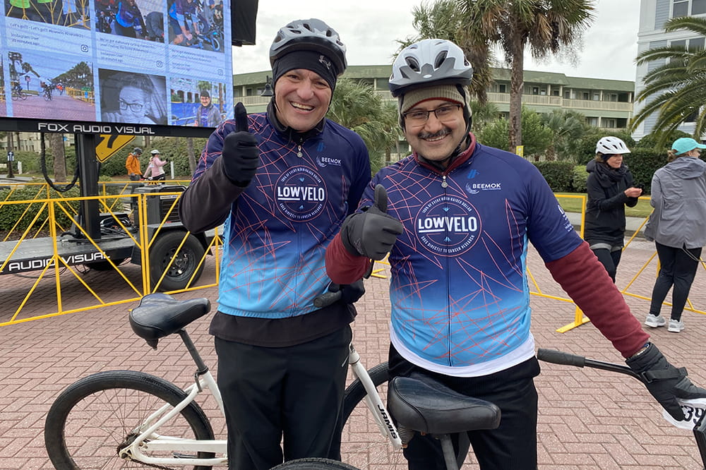two men in cycling jerseys and bike helmets give thumbs up in front of their bikes