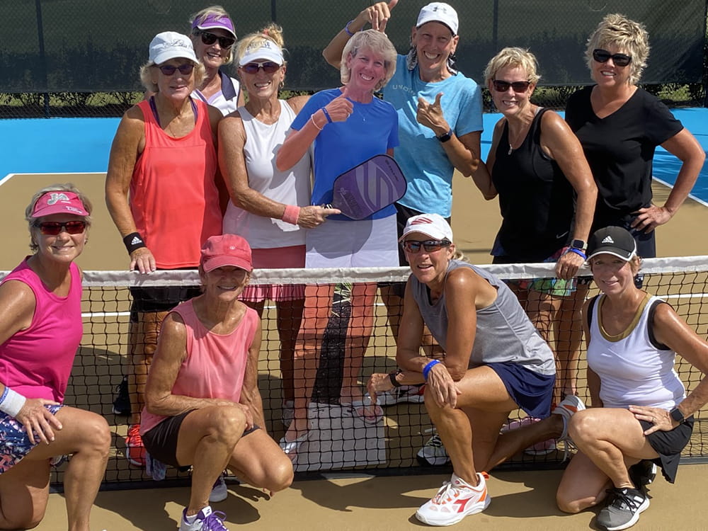 a pickleball team poses at the net with a cardboard cutout of one of the members