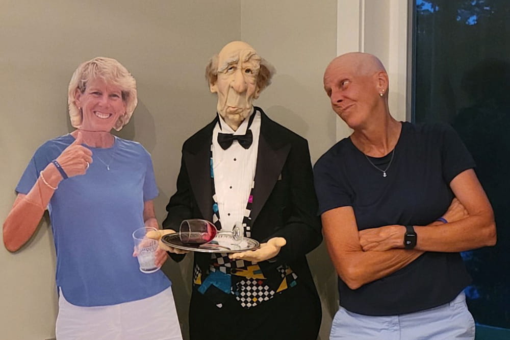  a woman with a bald head poses next to a life size butler mannequin and a lifesize cardboard cutout of herself with hair