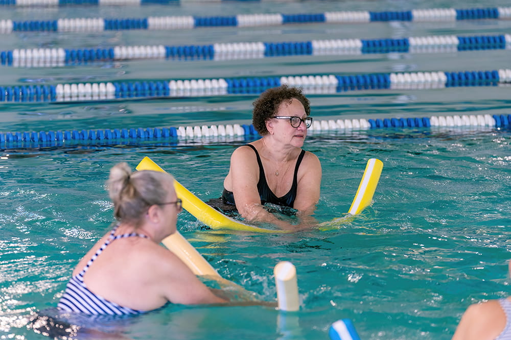 a woman holds a swim noodle below the water in a pool