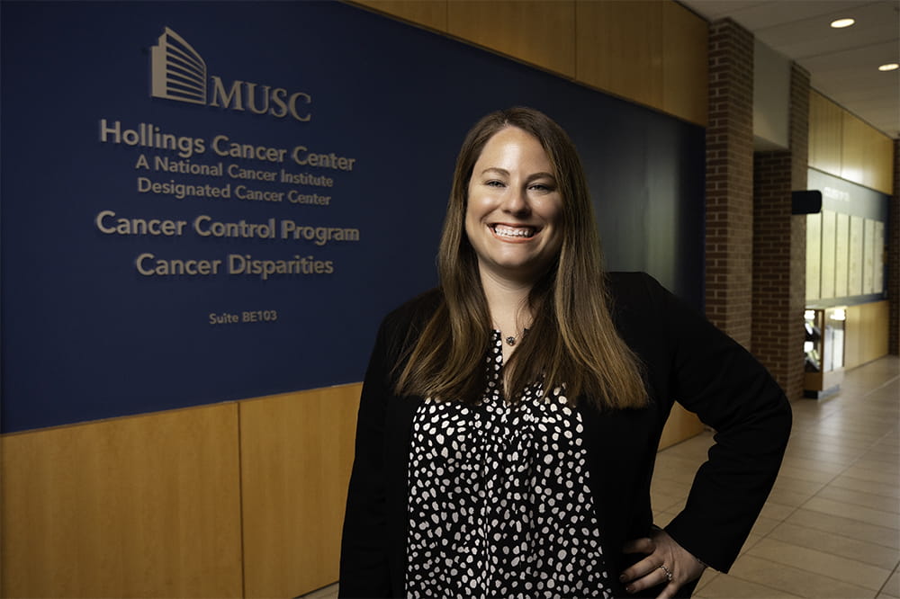 woman standing in a hallway smiling with sign on the wall that says Cancer Control